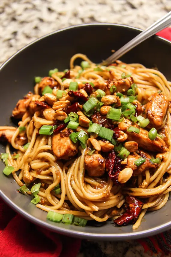 Kung pao chicken noodles served in a bowl with garnish