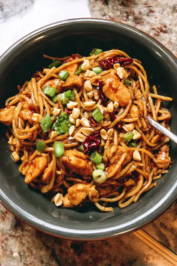 Homemade kung pao chicken noodles with sauce being stirred in a wok