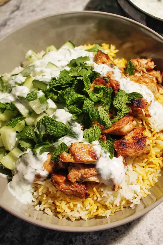 Creamy white sauce being drizzled over chicken shawarma rice bowl
