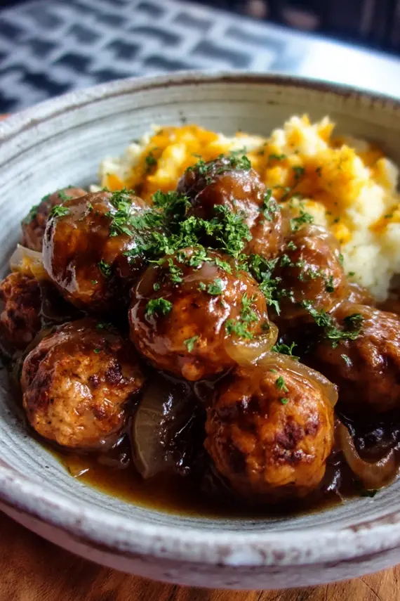 Meatballs with onion gravy served over mashed potatoes on a plate