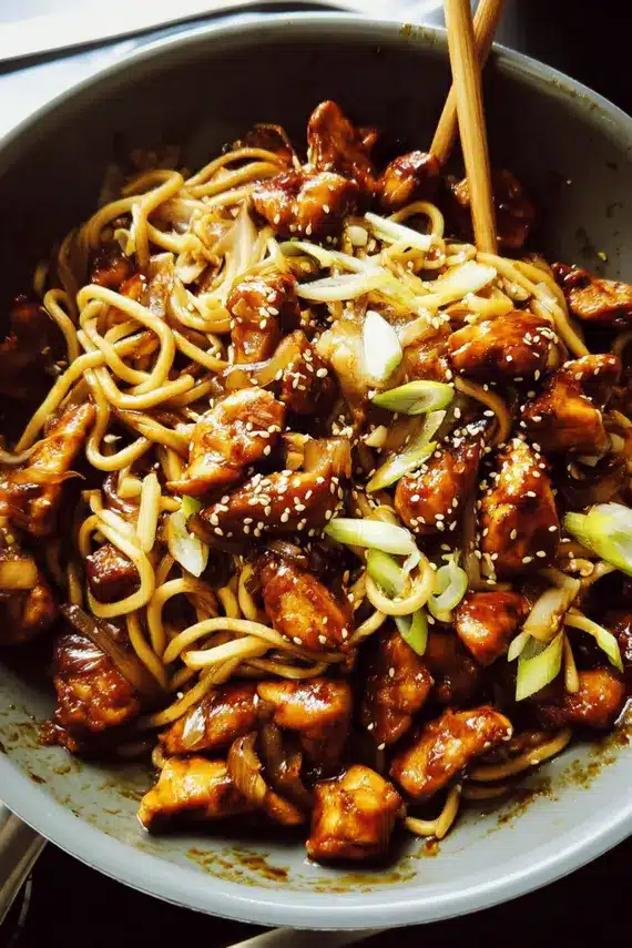 Sesame soy sauce being drizzled over chicken noodles in a wok